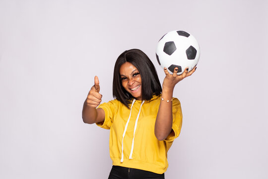 excited young black lady holding a soccer ball does thumbs up