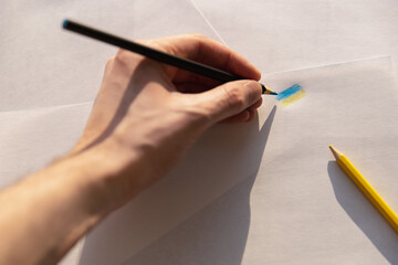 a man draws the flag of Ukraine with a colored pencil on a white sheet