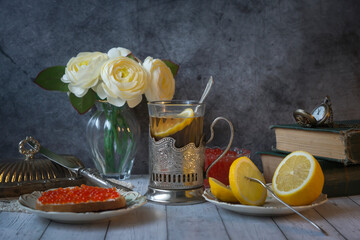 Still life in vintage style, tea with lemon in a faceted glass with a stand, caviar sandwich, sliced lemon. Still life in the style of the 40-70s.