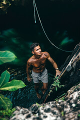 young tan male model climbing from a cenote in Tulum Mexico surrounded by green nature and a ladder