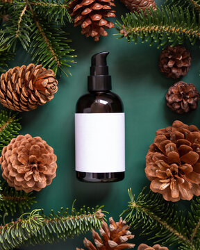 Brown glass dispenser near fir branches and pine cones on dark green top view. Brand packaging mockup.