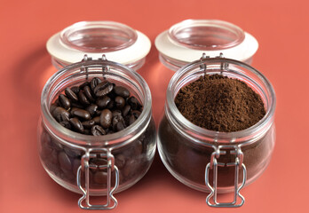 Roasted Coffee beans and grinded coffee in a glass jars close up on pink background
