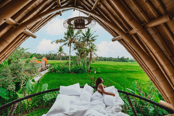 young asian female in a luxury bamboo eco villa overlooking the bali rice fields and coconut trees - obrazy, fototapety, plakaty
