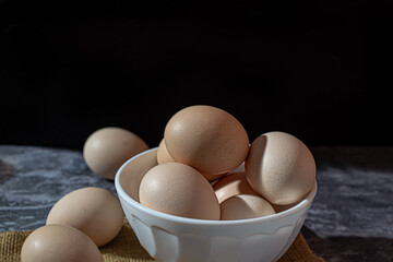 Close-up of raw chicken eggs in a white cup on a dark background
