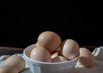 Close-up of raw chicken eggs in a white cup on a dark background