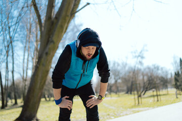 An athlete tired after running a few miles around the park. The man is bending over, breathing...