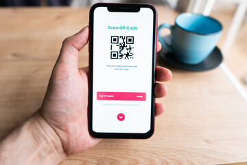 Young man in modern cafe showing smartphone scan QR code for payment 