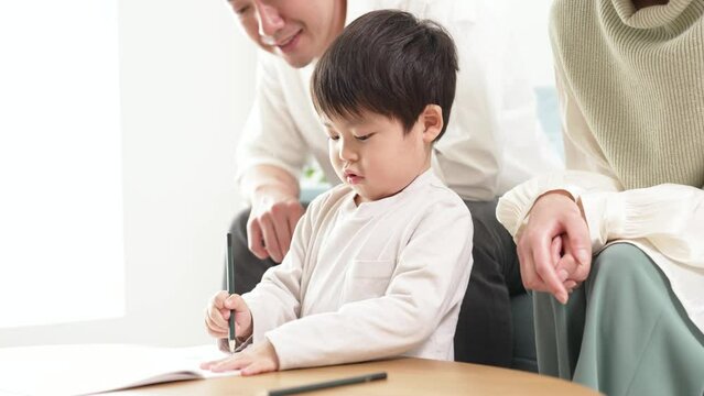 鉛筆を使ってお絵描きに取り組む男の子と、それを見守る両親