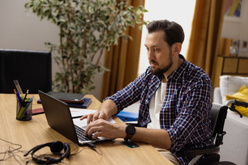 A middle-aged man sits in a wheelchair in his living room. The boy sends reports to his boss at the end of the day. Remote work at home. A modern room in the background