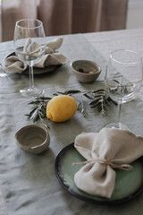 Elegance table setting in mediterranean style with linen tablecloth and napkins decarated with olive branches. Romantic dinner rustic centerpieces. Natural fabrics and simple country life