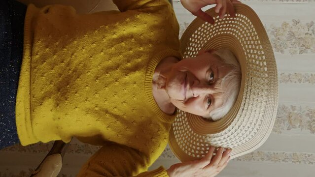 vertical video, seniour Caucasion lady posing looking at the camera and holding her hat, slowmotion. High quality 4k footage