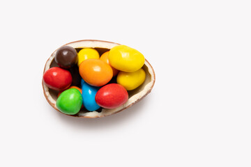 Cracked chocolate easter egg with colorful small round candies on white background, copy space, top...
