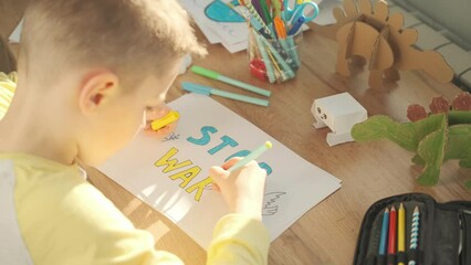 A little boy writes on paper a message to stop the war. No war, stop war concept video 4k.