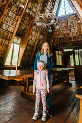 Obraz na płótnie Canvas Young mother and daughter standing in an old wooden house. Happy mother hugs the girl. Old wooden architectural house.
