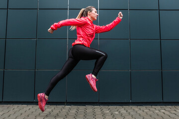 Young woman runner doing sports on sidewalk on modern background. Female model in sportswear exercising outdoors. Health concept, take care of yourself and your balance. Running outdoor.