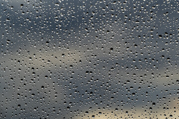 raindrops on a window pane with blurred dark clouds in the background