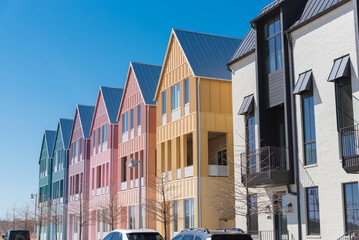 Row of multicolor brand new three-story houses with metal roofs against sunny clear blue sky in...
