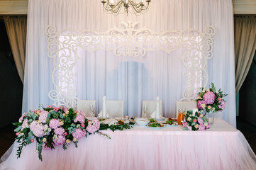 Festive table, arch decorated with composition of violet, purple, pink flowers and greenery, candles in the banquet hall. Table newlyweds in the banquet area on wedding party.