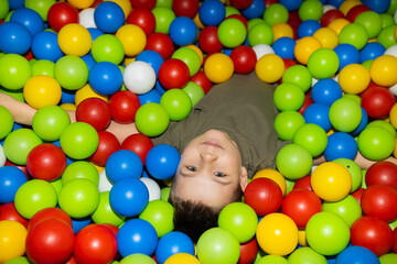 Fototapeta na wymiar Boy plays in dry pool. Multicolored plastic balls in dry paddling pool. Leisure activity in playroom at kindergarten. Leisure activity. Active recreation.