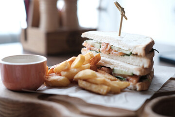 Salmon and cucumber sandwich with cheese sauce and french fries on a wooden board in a cafe. Business lunch or brunch. Horizontal photo. Selective focus.