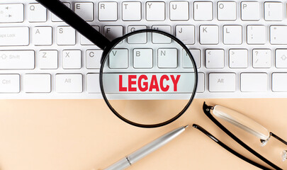 Text LEGACY on keyboard with magnifier , glasses and pen on beige background