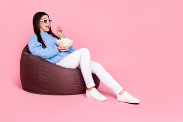 Portrait of attractive cheerful girl sitting eating pop corn enjoying tv show isolated over pink...