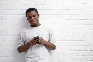 Black young man using smartphone over white brick background, finger, reading social media internet, typing text or shopping online, copyspace 