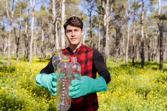 volunteer man picks up plastic rubbish in forest, Young activist cleaning up rubbish park - Powered by Adobe