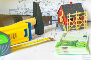 Private house model, construction tools, measuring instruments, money and blurred  house drawings in the background. Private house design and construction costs