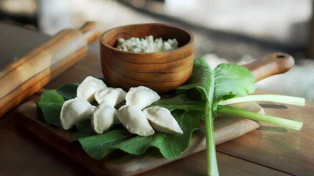 Traditional Russian fresh handmade dumplings lying on a wooden table on a cutting board with cottage cheese in a wooden plate and spinach