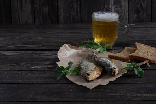 salted, dried vobla fish with amber beer on a dark wooden background with bread on table, with copy space