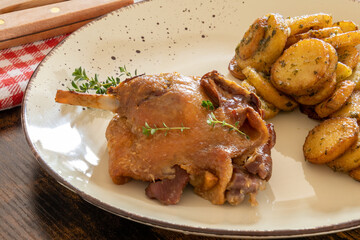 view of a duck leg confit with sarladaise potatoes on a plate