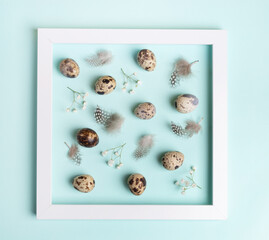 White square frame, quail eggs, feathers, gypsophila inside it on light blue. Easter poster idea.