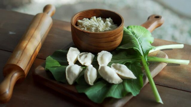 Traditional Russian fresh handmade dumplings lying on a wooden table on a cutting board with cottage cheese in a wooden plate and spinach
