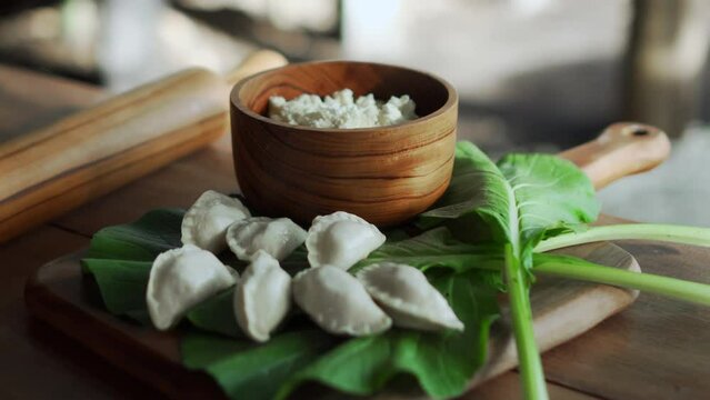Traditional Russian fresh handmade dumplings lying on a wooden table on a cutting board with cottage cheese in a wooden plate and spinach