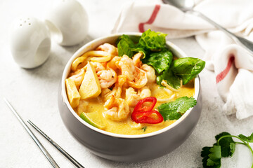 Asian laksa soup with shrimp in a ceramic bowl on a light culinary background. Spicy broth soup with coconut milk, rice noodles and seafood in a plate on the closeup kitchen table closeup