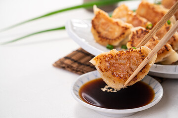 Pan-fried gyoza dumpling jiaozi in a plate with soy sauce on white table background.