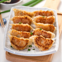Pan-fried gyoza dumpling jiaozi in a plate with soy sauce on white table background.