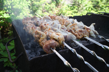 Meat is sliced and cooked on skewers on the grill outdoors.
