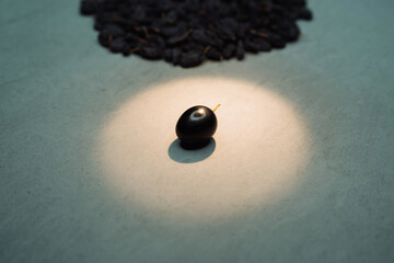 One grape on a gray table with a directional light on it with a bunch of raisins in the background....