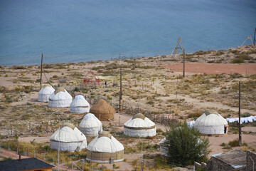 Camp with white yurts against the blue sky and hills on the shore of Lake Issyk-Kul in Kyrgyzstan