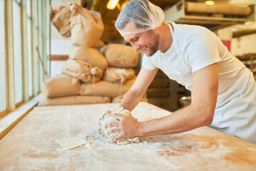 Young man as a baker in training kneading the dough - obrazy, fototapety, plakaty