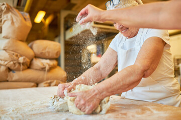 Two bakers knead the dough and sprinkle flour