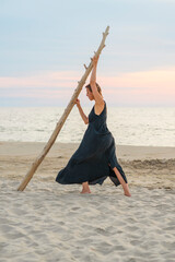 Woman in black dress with wooden snag on the seashore - 498509101