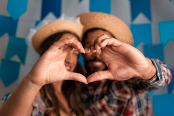 Festa Junina in Brazil, close up of couple hands making heart shape at brazilian june festival...