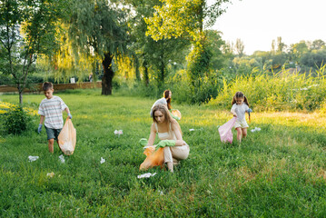 A group of adults and children together at sunset is engaged in garbage collection in the park....