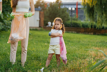 A little girl is upset about cleaning garbage in the park during sunset. Environmental care,...