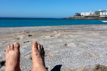 Men's feet in the sand against the background of the ocean shore.