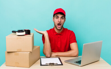 hispanic handsome man looking surprised and shocked, with jaw dropped holding an object. packer...