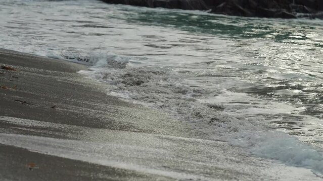A close-up shot of the long tidal waves spilling on the sandy shore. Slow-motion.